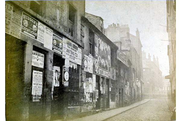 This view shows the east side of Low Vennel opposite Hunter Place, Greenock showing a street of dilapidated houses covered with advertising posters. - P4214 © McLean Museum and Art Gallery, Greenock