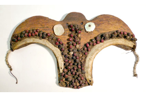 A late 19th century pectoral ornament or Musikaka, from Papua New Guinea in the form of a wooden bird decorated with Abrus seeds and mother-of-pearl. The seeds, shell and mother of pearl are fixed on to the wooden base by means of an adhesive, possibly a natural resin and pins. - 1981.509 © McLean Museum and Art Gallery, Greenock.