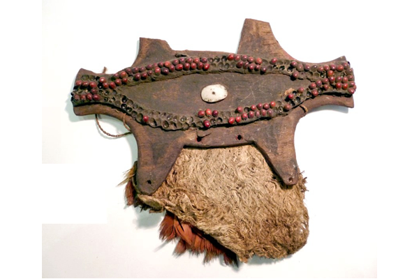 A late 19th century pectoral ornament or Musikaka from Papua New Guinea in the stylised form of a quadruped animal, possibly a flying fox. The wooden base decorated with Abrus seeds, shell and with a tapa cloth pouch with feathers fixed to it by cord. - 1981.508 © McLean Museum and Art Gallery, Greenock.