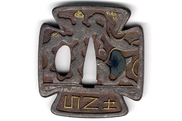 A Japanese swordguard or tsuba, date unknown. It has an archaic design of dragons and Greek fret, in relief and inlaid with precious metals. One side of the tsuba is decorated with bonji figures, carved and gilded. - 1981.62 - © McLean Museum and Art Gallery, Greenock