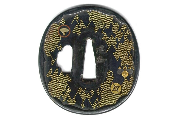 A Japanese swordguard or tsuba, date unknown. The design shows a gilded saya pattern with mons and swastikas including flowers and the Kiri mon and leaves. - 1981.80 - © McLean Museum and Art Gallery, Greenock