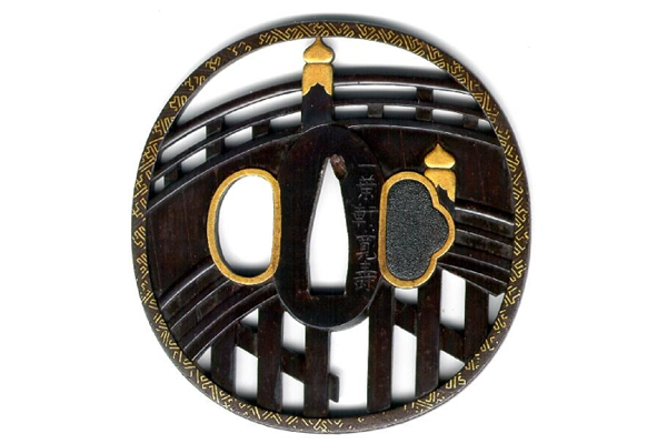 A eighteenth century Japanese swordguard or tsuba. The design is in openwork and shows the sacred bridge with saya border pattern (gilded) engraved with gold inlays. The inlays are signed 'Shoyetsu a pupil of Goto Seijo.' The tsuba is signed: 'Ichyo-ken Kuanju.' - 1981.96 - © McLean Museum and Art Gallery, Greenock