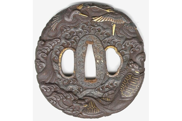 A Japanese swordguard or tsuba, date unknown. The design shows a central area of turbulent waves with storks and the giant hairy tailed tortoise on the rim. - 1981.107 - © McLean Museum and Art Gallery, Greenock