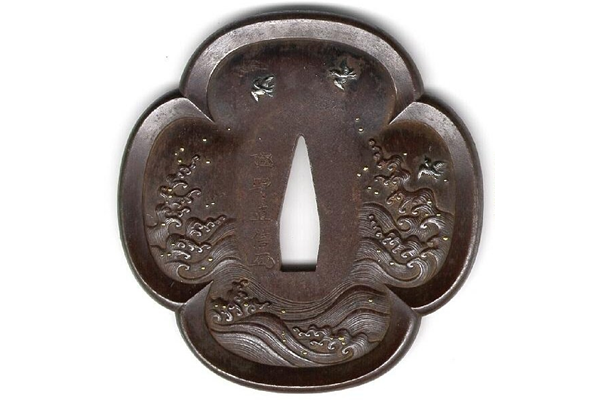 A eighteenth century Japanese swordguard or tsuba. The design shows turbulent water with birds in flight, carved in relief and inlaid in gold and silver. Signed: Nawonobu Takeno. - 1981.113 - © McLean Museum and Art Gallery, Greenock