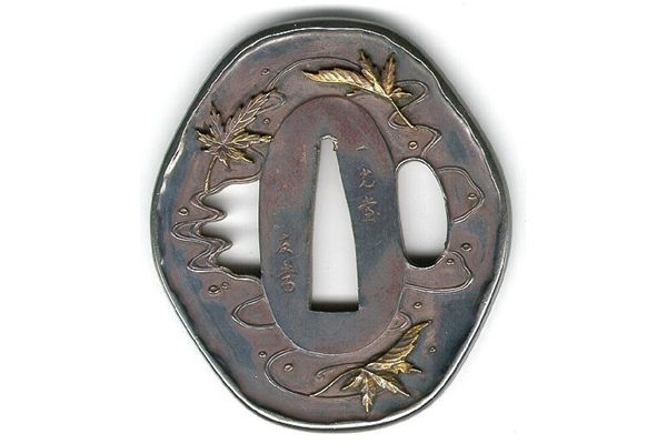 A very late nineteenth century Japanese swordguard or tsuba. The design shows maple leaves and cherry blossoms in relief and inlaid with precious metals. Dated 1900. Signed: Tomotsune. - 1981.129 - © McLean Museum and Art Gallery, Greenock