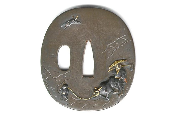 A Japanese swordguard or tsuba, date unknown. The design shows a farmer with a bullock led by a boy with a crane in flight above. - 1981.157 - © McLean Museum and Art Gallery, Greenock