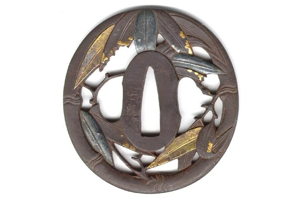 A eighteenth century Edo period Japanese swordguard or tsuba. The design shows the rim as a bamboo frame with a design of leaves with inlays & gilding on both faces. Signed: Yasuchika. - 1981.142 - © McLean Museum and Art Gallery, Greenock