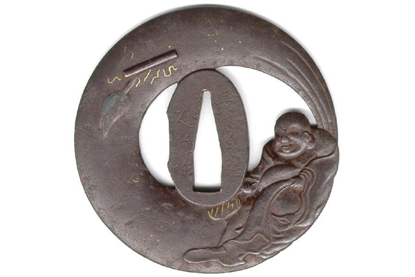 A eighteenth century Japanese swordguard or tsuba. The design shows Hotei Osho with his treasure bag in relief casting and openwork. Decorated with gold and silver inlays. Signed: Tomomitsu. - 1981.125 - © McLean Museum and Art Gallery, Greenock