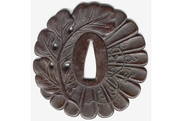 A Japanese swordguard or tsuba, date unknown. the circular form is in the shape of a chrysanthemum leaf and vine carved on both faces with gilding. - 1981.105 - © McLean Museum and Art Gallery, Greenock 